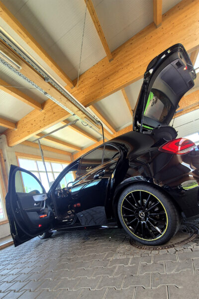 Ein Auto der Marke Mercedes steht mit offener Tür und Heckklappe in einer Indoor-Reinigungshalle